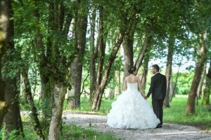 A rear view of the bride and groom holding hands, looking at each other and walking down a pathway in the forest.